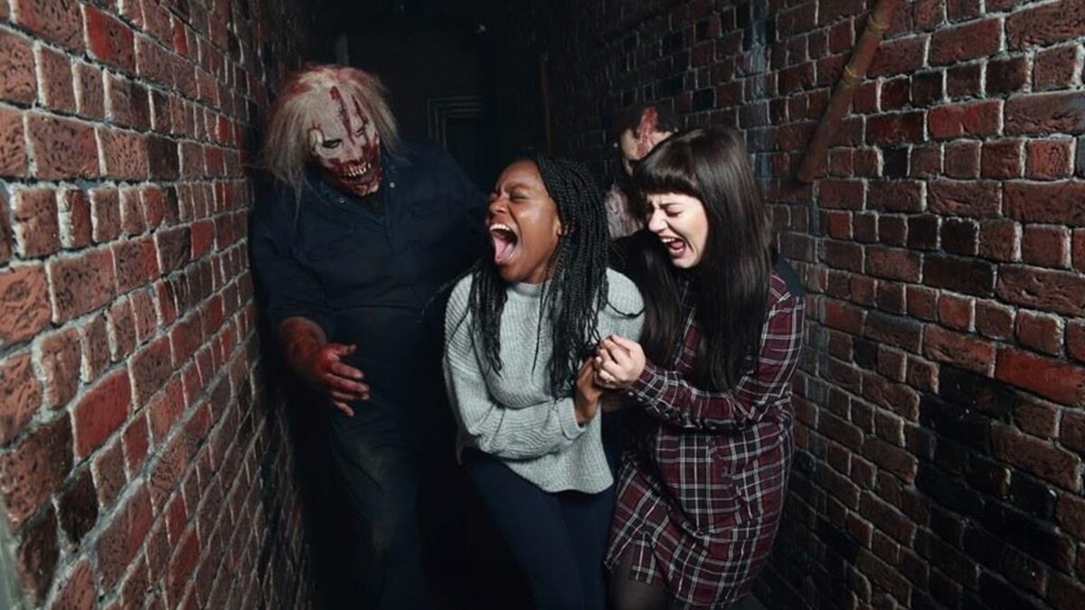 Visitors screaming in a brick corridor as a masked actor lunges, from Thorpe Park's Fright Nights